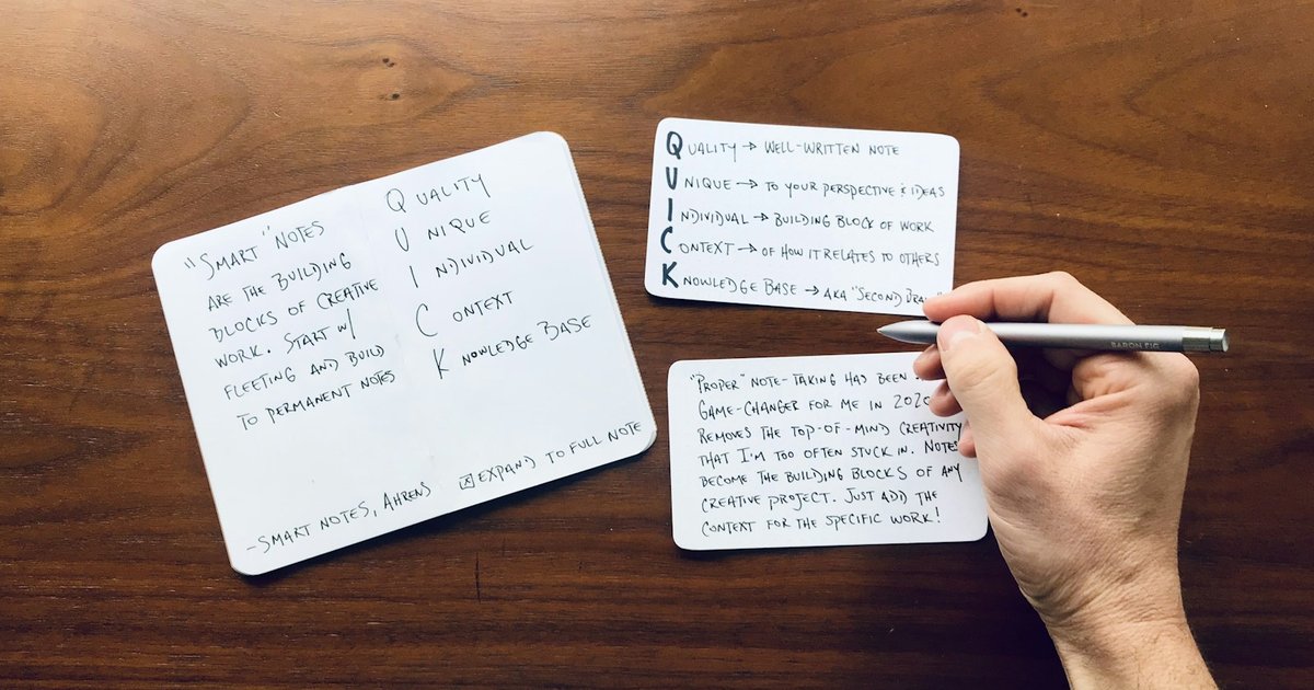 Hand writing study notes on small white index cards laid out on a dark wooden desk