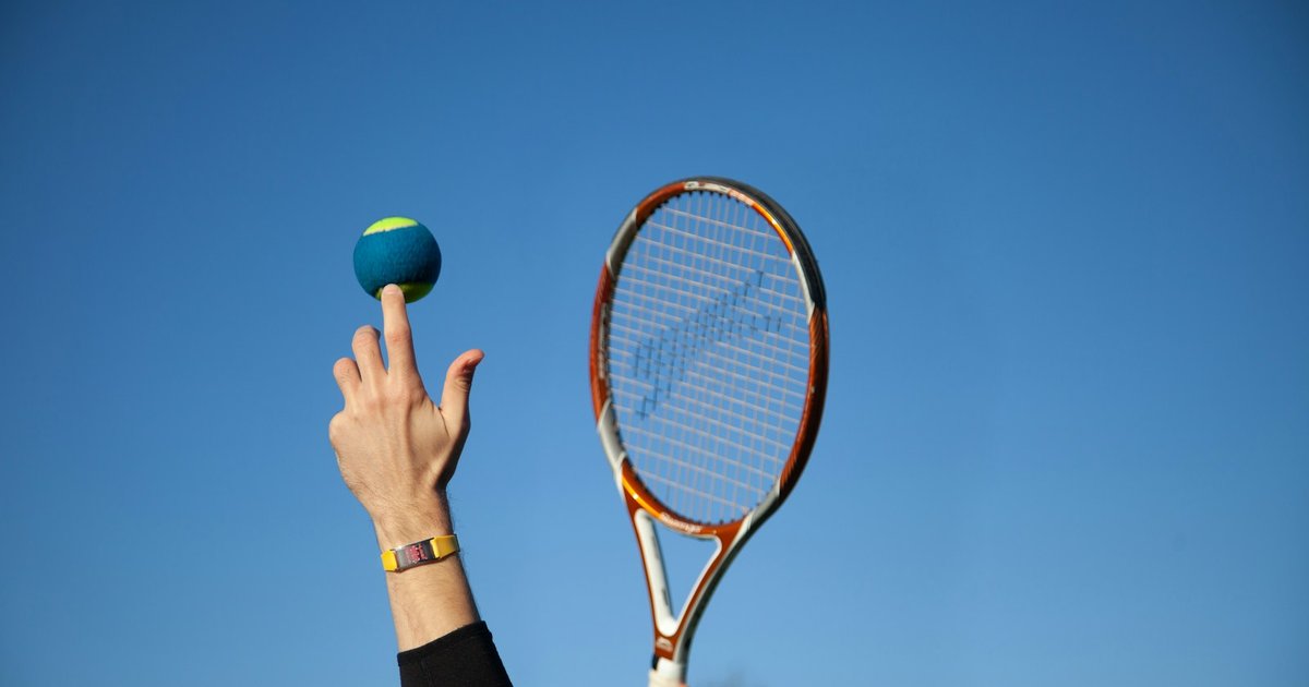 A tennis player tossing a ball into a clear blue sky with a racquet raised to serve