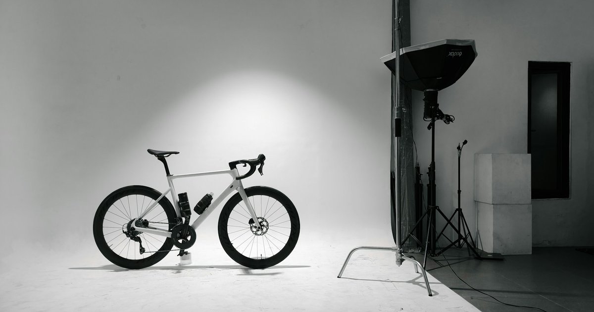 A white road bike on a seamless white studio sweep, lit by a softbox on a stand